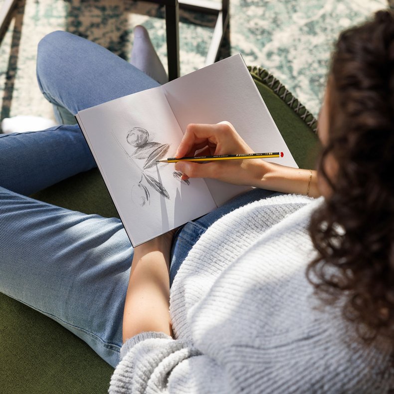 Eine Frau skizziert in ein Notizbuch mit Bleistiften von Staedtler