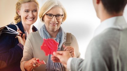 Zwei Kundinnen der Sparkasse Fürth erhalten ein kleines rotes Schweinchen.