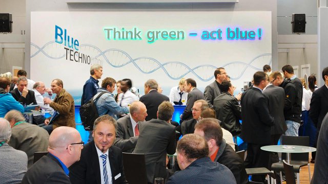 Blick auf den Messestand von Sumitomo. Im Hintergrund sieht man eine Wandgestaltung mit dem Claim: Think green - act blue.