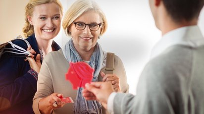 Zwei Kundinnen der Sparkasse Fürth erhalten ein kleines rotes Schweinchen.