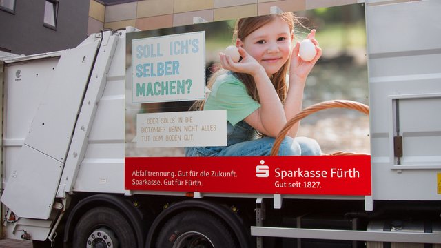 Ein Müllauto beklebt mit einem Motiv der Abfallwirtschaft Fürth: Ein Mädchen hält zwei weiße Eier in den Händen.
