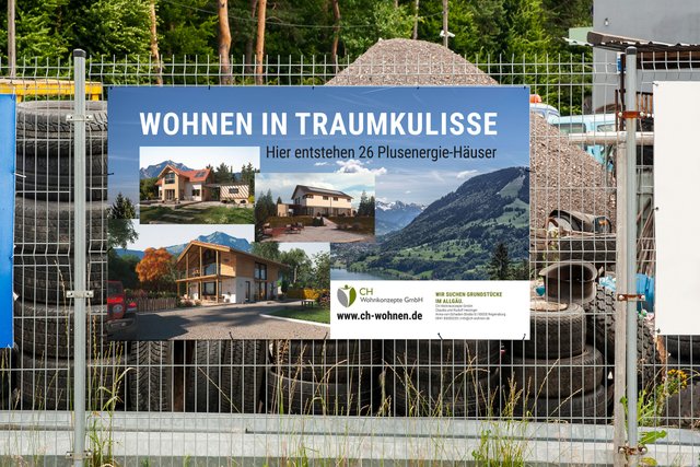 Ein Bauzaun-Banner von CH Wohnen hängt an einem Zaun vor einem großen Erdhügel.