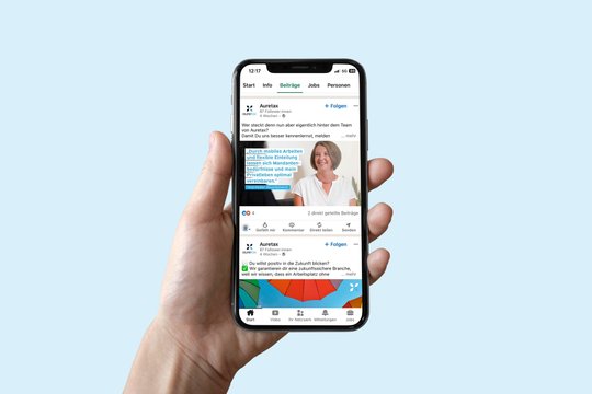 Eine Hand hält ein Smartphone hoch auf dem die LinkedIn Seite von auretax zu sehen ist. 