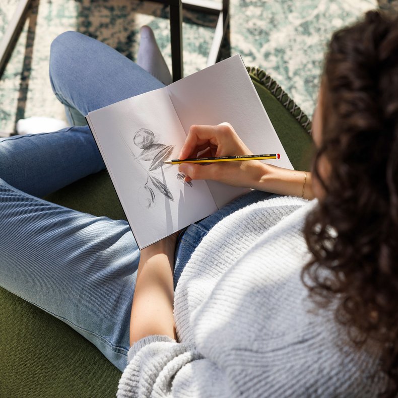 Eine Frau skizziert in ein Notizbuch mit Bleistiften von Staedtler