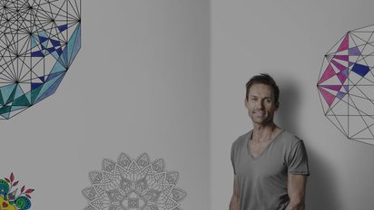 Sven Hannawald lehnt an einer Wand auf der halb ausgemalte Mandalas zu sehen sind 