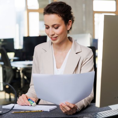 Eine Frau sitzt in ihrem Büro am PC und markiert Blätter