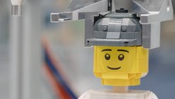 Ein Legomännchen wird von einem Roboter zusammengesteckt.