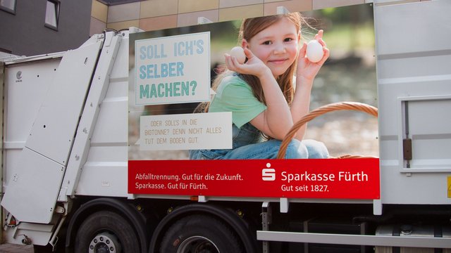 Ein Müllauto beklebt mit einem Motiv der Abfallwirtschaft Fürth: Ein Mädchen hält zwei weiße Eier in den Händen.